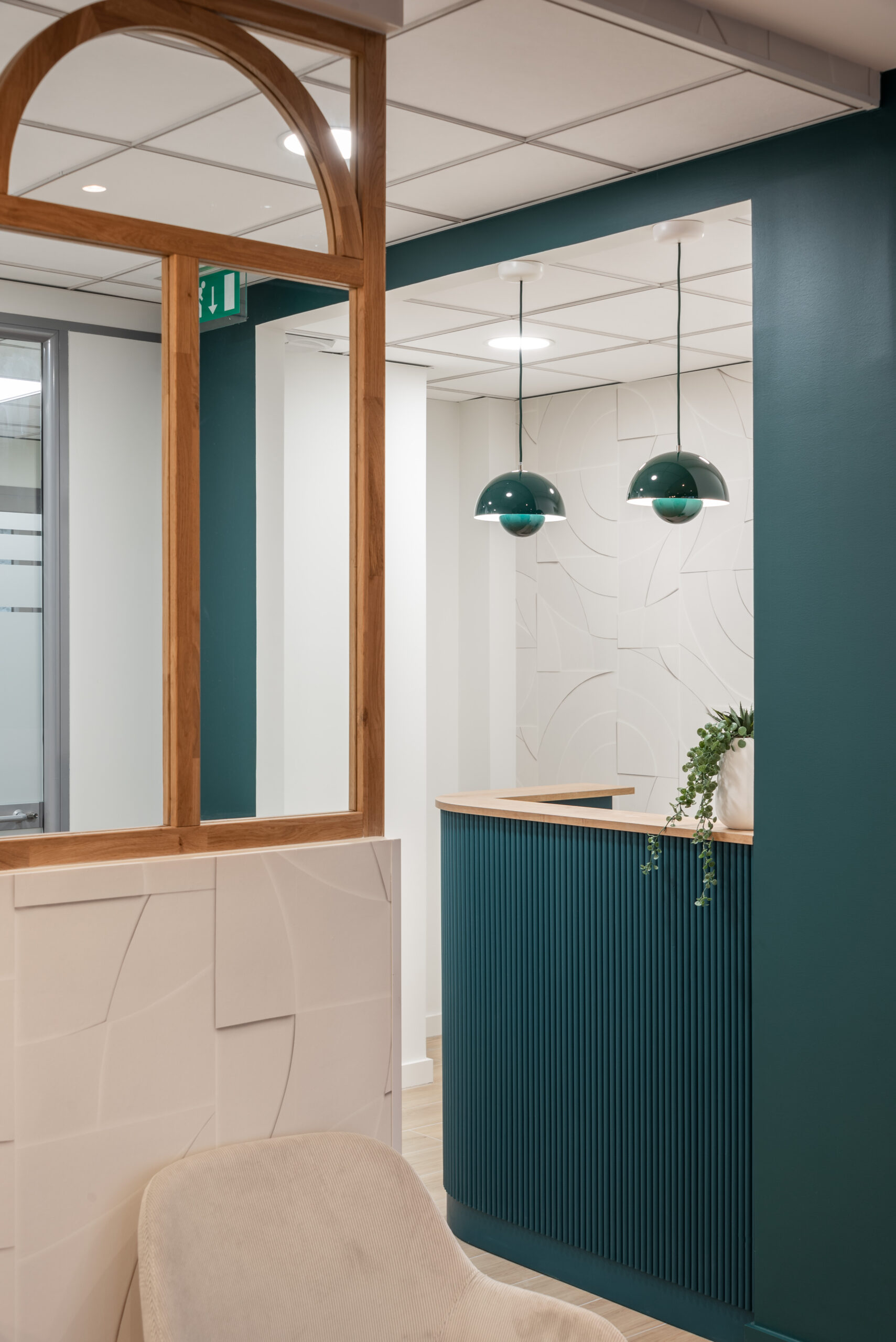 Projet ONE – Comptoir d’accueil chic avec suspensions vert foncé et mur texturé Comptoir d’accueil sur mesure avec suspensions design vert foncé et mur texturé, office notarial aménagé par Julie Porcella Aménagement d’un espace professionnel en Isère – Jolis Projets.