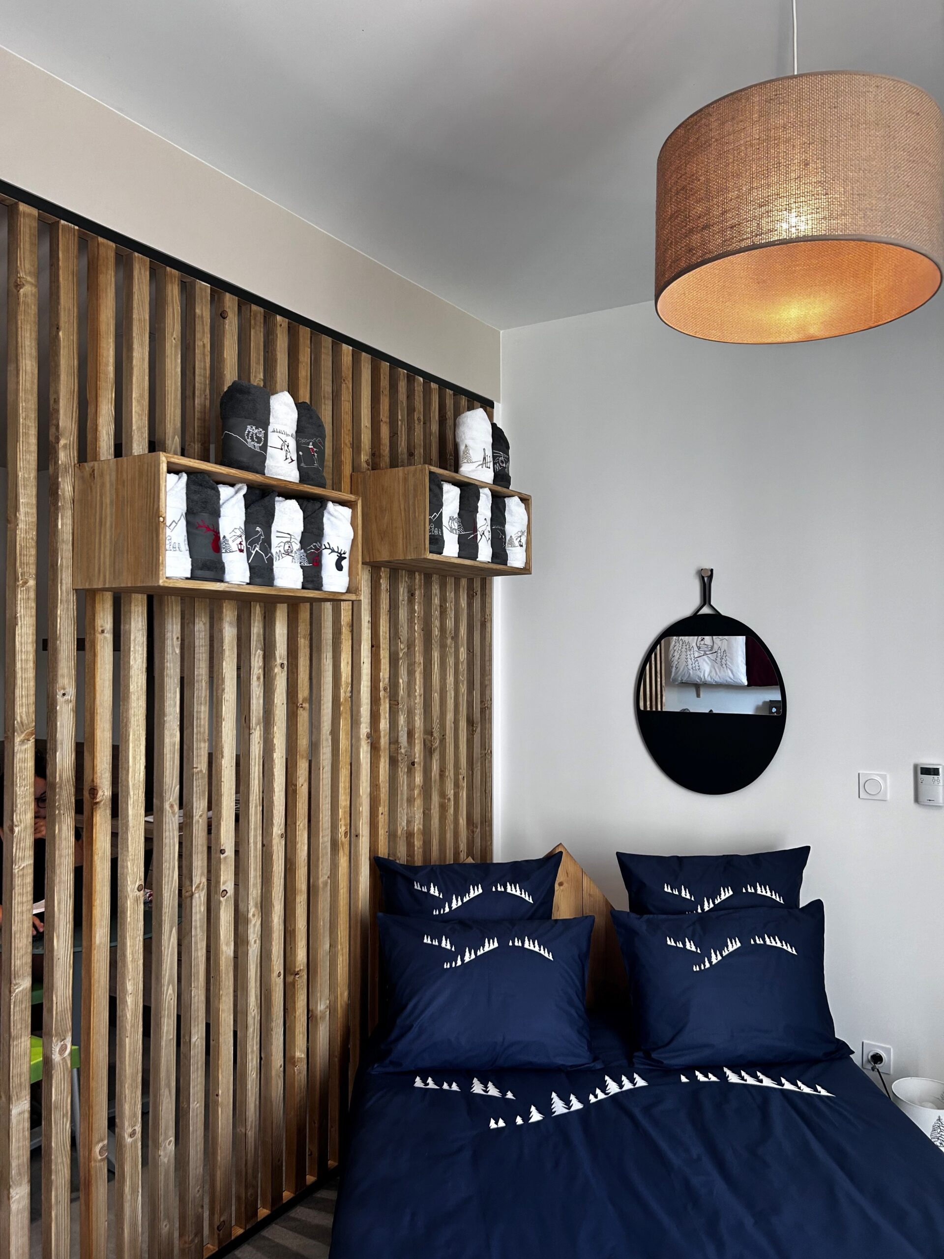 Linge de lit bleu nuit ambiance montagne – showroom Projet V.I par Julie Porcella décoratrice Grenoble Isère Chambre showroom avec linge de lit bleu nuit motif sapins et claustra bois – projets décoration intérieure professionnels Isère